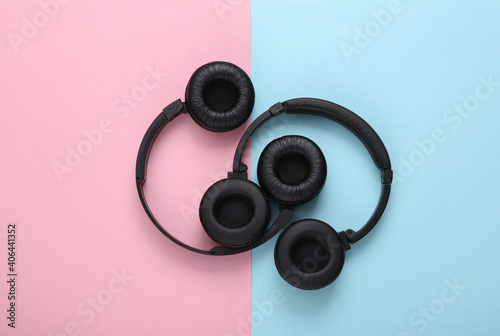 Two pairs of black wireless stereo headphones on a blue pink background