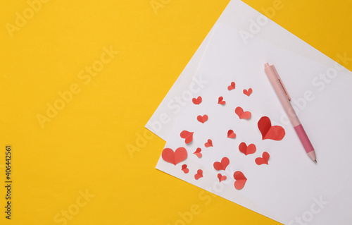 Handmade paper-cut red hearts, pen and letter on yellow background. Valentia day concept. Love letter