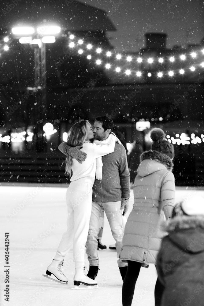 Happy couple of lovers having fun, hugging an kissing at ice skating rink outdoor. St. Valentines Day, Winter leisure, New Year holidays concept.