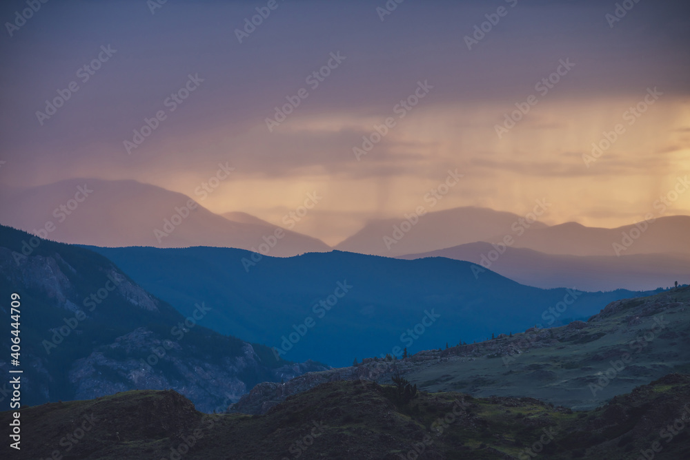 Atmospheric landscape with silhouettes of mountains with trees on background of vivid orange blue lilac dawn sky. Colorful nature scenery with sunset or sunrise of illuminating color. Sundown paysage