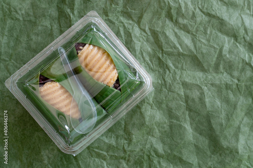 Transparent plastic box containing Thai sweets Sticky Rice with Thai Custard or Khao Neeo Sankaya Wrapped in banana leaves. Crumpled paper green color for background. photo