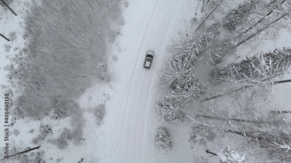 Aerial tracking shot of a suv car on snowy road turning right in middle of snow covered trees in frozen forest, on a winter day - drone shot, tracking, top down