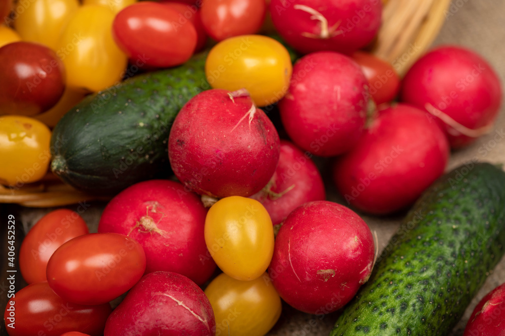 Green cucumbers, ripe radishes and colorful tomatoes scattered on the table. Close-up, selective focus.