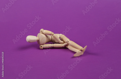 Scared or stressed wooden puppet lies on purple background