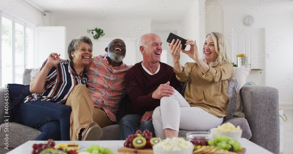 Two diverse senior couples sitting on a couch using a smartphone and laughing