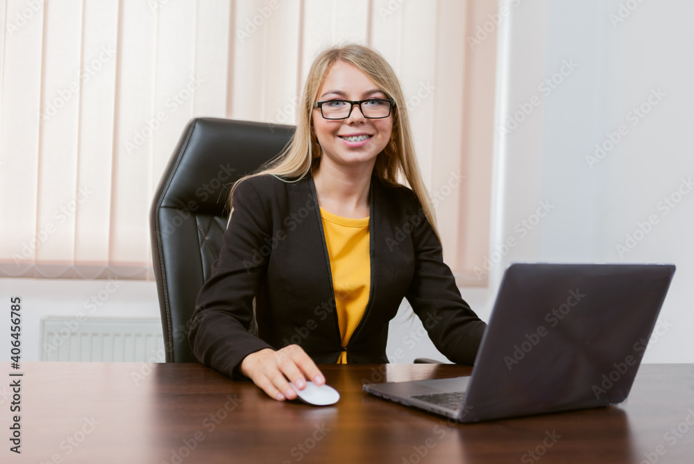 Portrait of a female boss in a jacket in her office. Business lady is sitting at table with laptop. Portrait of a female boss in a jacket in her office. Business lady is sitting at table with laptop.