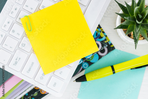 Yellow sheet of paper with space for text. Office accessories, computer keyboard, pens, documents on the desk