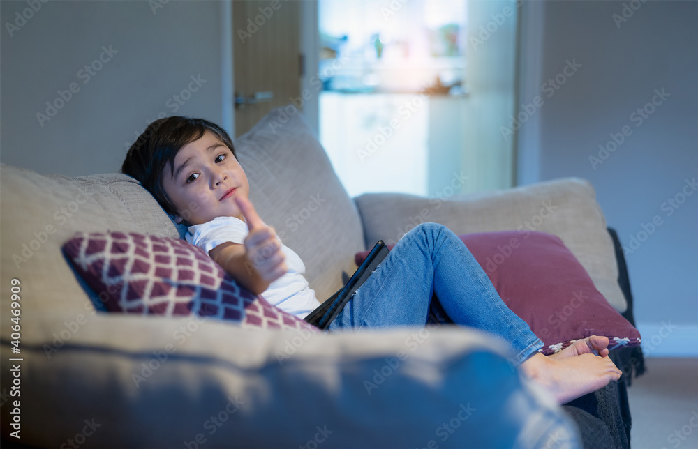 Kid with blurry thumb up,Selective focus Child sitting on sofa with smiling face.Boy stay at home using tablet learning online lesson from school,Home school,Distance education,E-learning concept