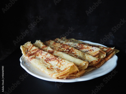 Homemade crepes, french crêpes, traditionally made for Candlemas, on black background, showing the whole plate, horizontal picture and space for text