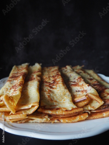 Homemade crepes, french crêpes, traditionally made for Candlemas, on black background, vertical picture and space for text