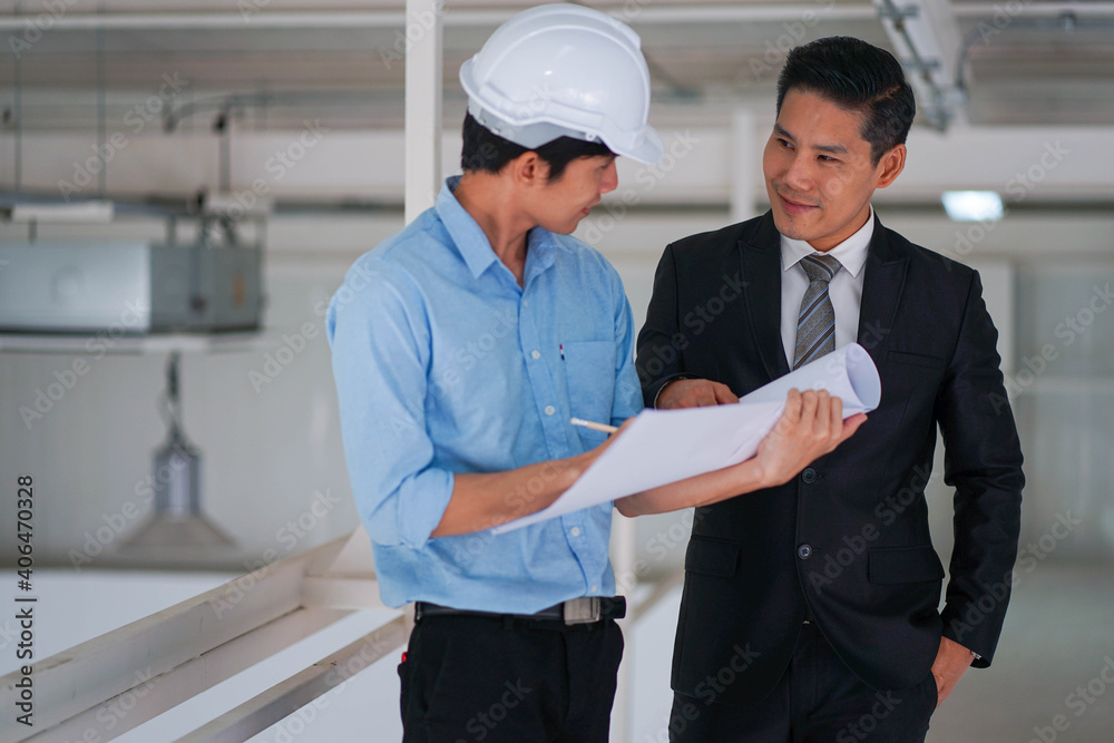 Asian engineer wearing hard hat talking with business man in formal suit in the factory