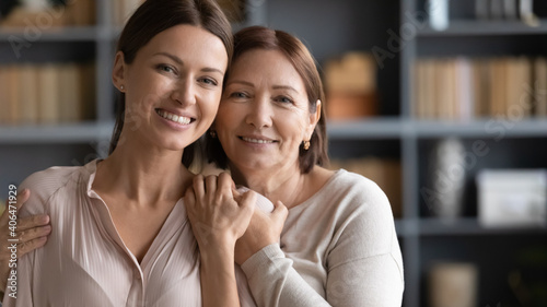 Head shot portrait happy two generations of women hugging, standing at home, smiling mature elderly mother embracing beautiful grownup daughter from back, family posing for photo together photo