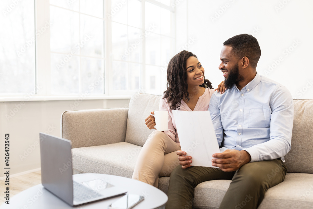 Positive black couple reading documentation at home, checking agreement Positive black couple reading documentation at home, checking agreement