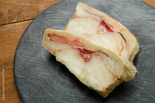 Fresh cod fish steaks on a black round board.