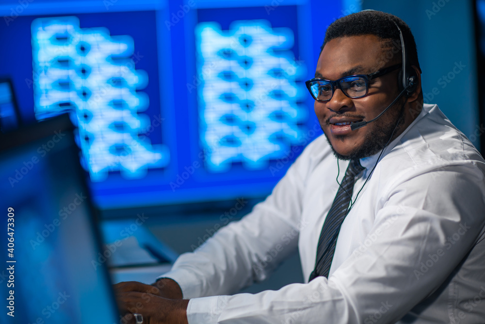 Call-center worker is speaking with the client by headset. Workplace of the african-american support operator.