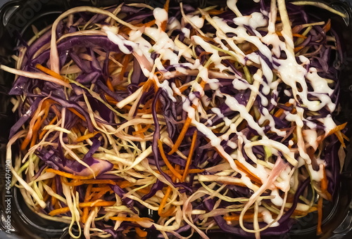 Red and white cabbage salad with carrots, decorated with white yogurt close-up on a black plastic backing