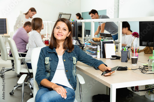 Young smiling glad friendly cheerful woman sitting at her workplace in office.