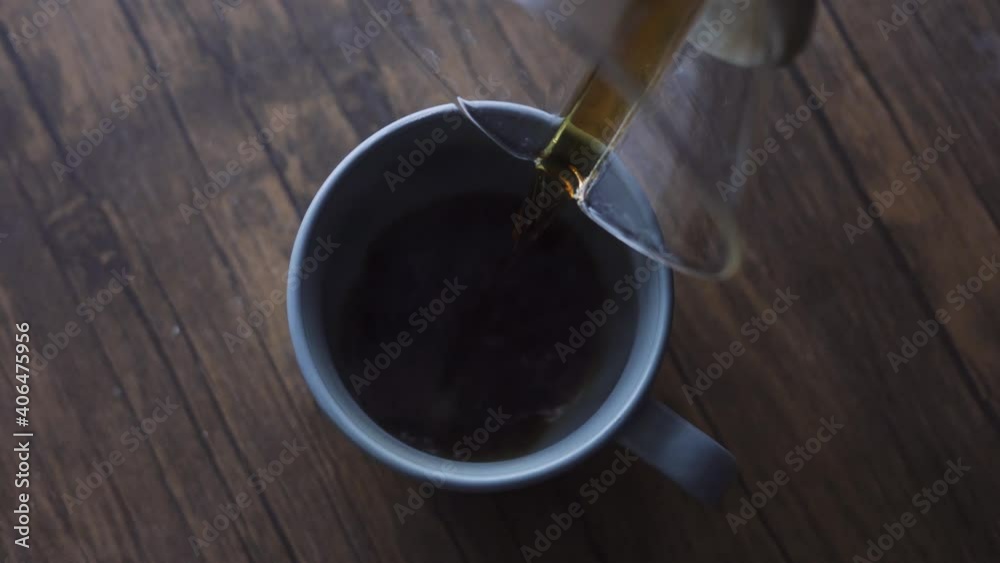 Pouring hot coffee, obtained by infusion, from a glass jar into a cup. Above overhead handheld shot. Pouring hot coffee, obtained by infusion, from a glass jar into a cup. Above overhead handheld shot.