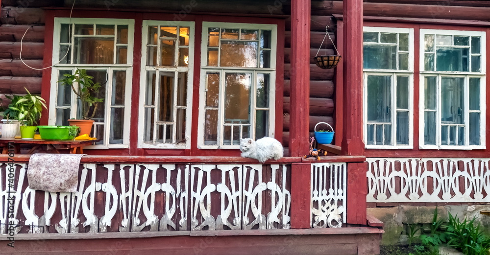 White cat on the railing on the background of the facade of a red wooden house White cat on the railing on the background of the facade of a red wooden house
