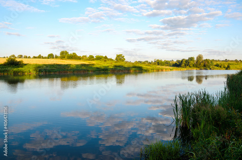 Summer tranquil landscape with river and beautiful reflection of sky clouds on water surface.