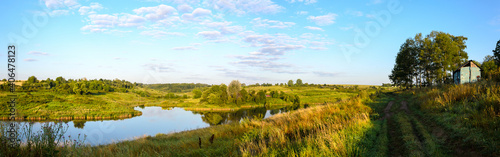 Sunny panoramic coyntryside landscape with rural road and calm river during august morning