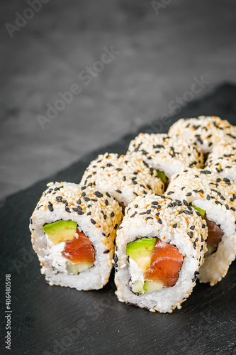 appetizing california sushi roll with cheese avocado cucumber and salmon in sesame seeds on a black stone plate