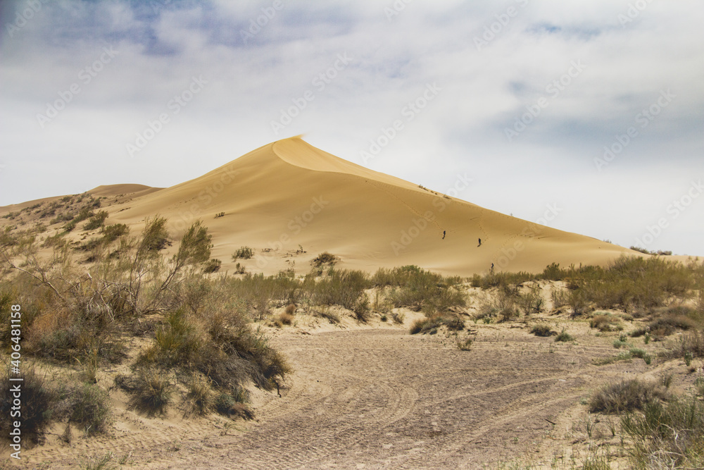 Sand dune against the blue sky. Against the background of a cloudy sky, a sand dune in the desert, sunny summer day, the road in the sand