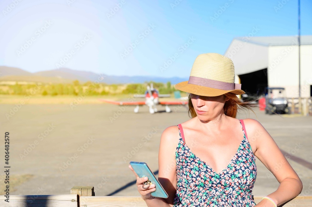young woman in dress and hat taking selfie with mobile on the airfield