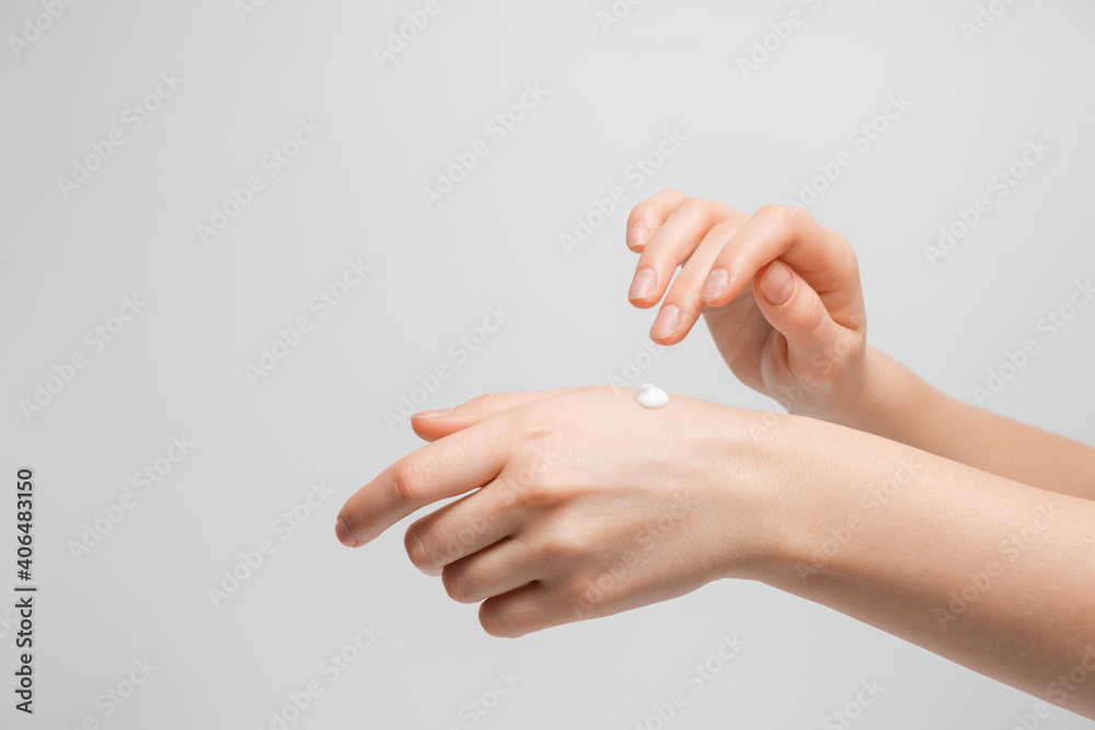 Beautiful young woman hands with cream. Woman applies cream on her hands on grey background. Palms down with smooth skin on hands, nice natural short nails.