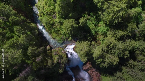 AERIAL shot of sunny turqoise water flowing and falling from lush green forest waterfall photo