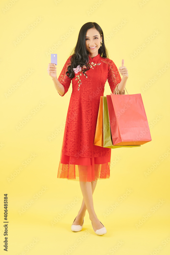 Beautiful young Asian woman showing credit card and shopping bags with purchases she made