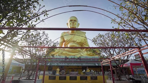 4k Panning backward from a golden statue of a monk Luang Pu Thuat. Big Golden Statue in mountains at beautiful sunrise in Khao Yai, Korat province. Sun glare at dawn photo