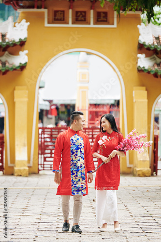 Cheerful young Asian couple with blooming peach branches visiting temple to celebrate Lunar New Year © DragonImages