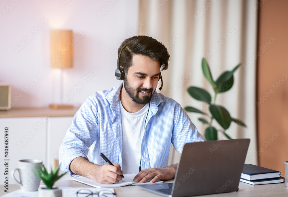 Online Education. Young Arab Guy Watching Webinar On Laptop And Taking Notes Online Education. Young Arab Guy Watching Webinar On Laptop And Taking Notes