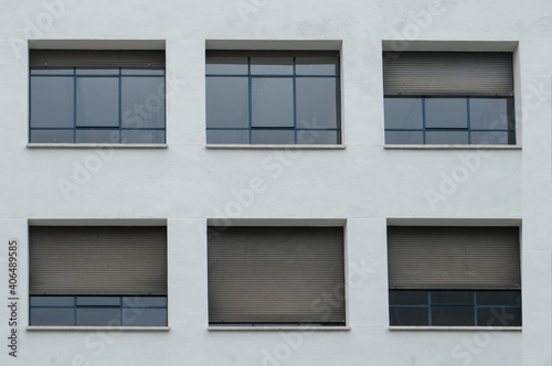 white facade with six rectangular windows with the shutters lowered to different heights