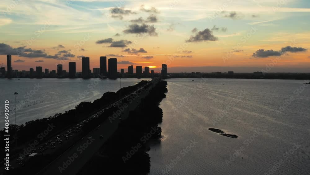 Sunset behind metropolitan Miami Florida skyline, golden hour, backlit clouds, purple skies, aerial dolly back