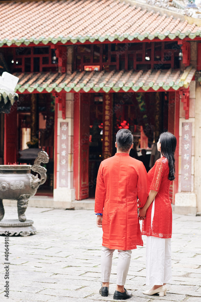 Young Vietnamese couple in traditional clothes looking at old temple when walking outdoors on Lunar New Year