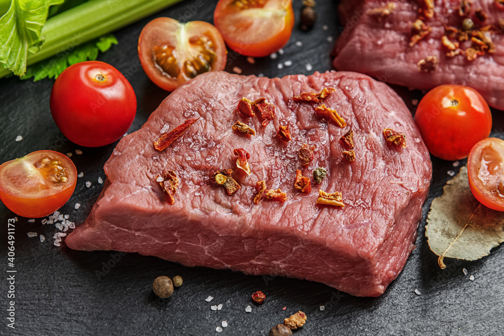 fresh raw meat with cherry tomatoes, spices and herbs on a black slate surface