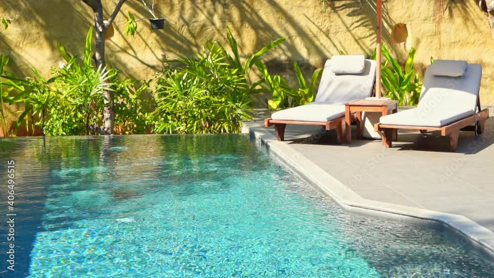 Luxury lounge area for a couple rest with two deck chairs and umbrella next to the swimming pool surrounded with green plants background
