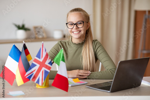 Happy teen girl sitting at home using laptop, studying languages photo