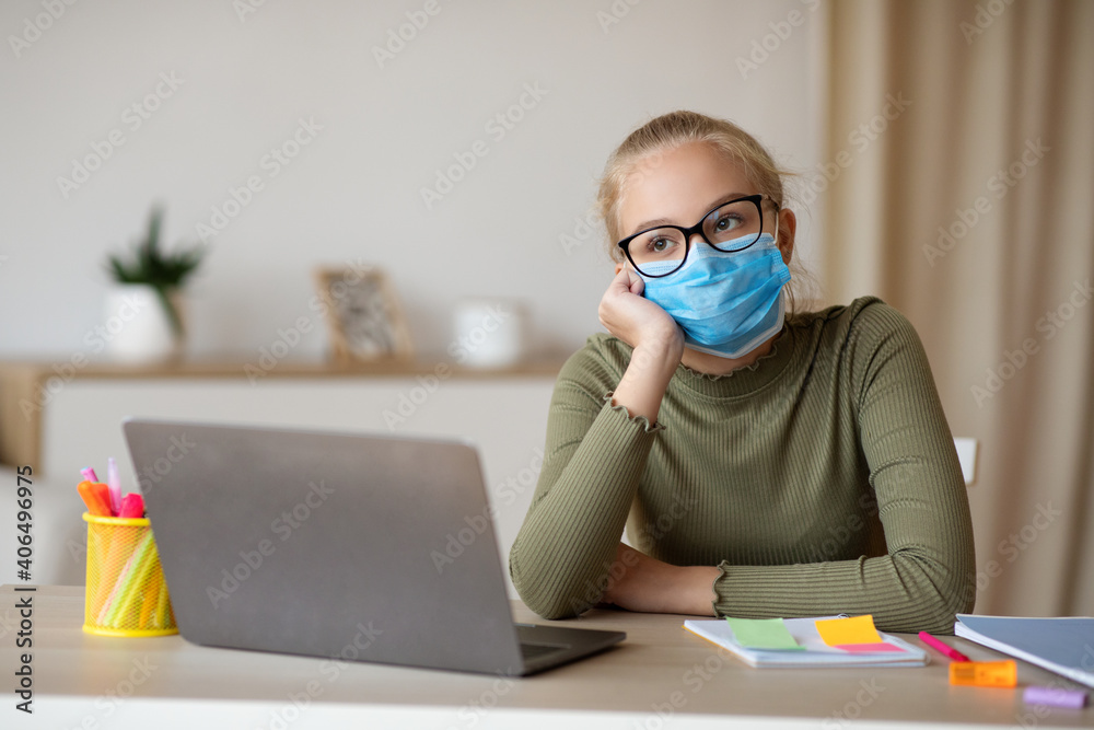 School girl in face mask sitting in front of laptop