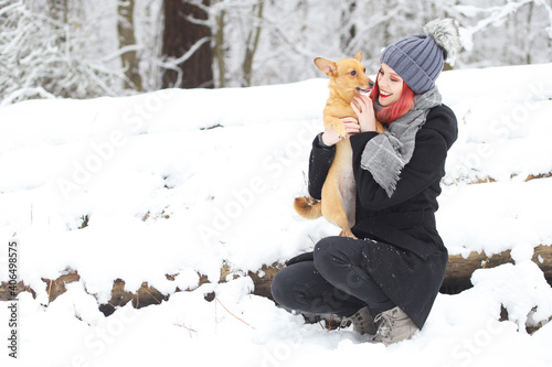 Smiling attractive red hair girl is cuddling with her brown dog in wintry snovy nature. photo