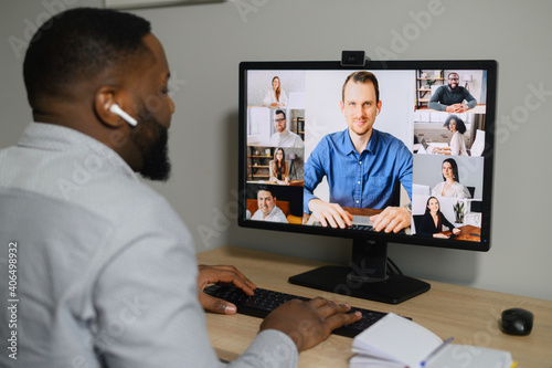Training, webinar online. A young African guy is watching on the screen with a group of diverse people on it. Multiracial team have online meeting, virtual conference