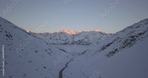 Aerial view over winding, mountain roads, revealing a range of sunlit, alpine peaks, sunset, in Austria - tilt up, drone shot photo