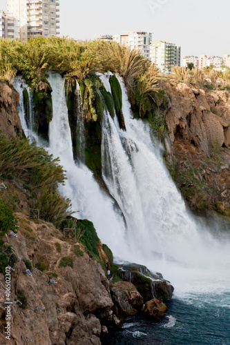 A waterfall erupts into the sea from a great height on a sunny day near the city