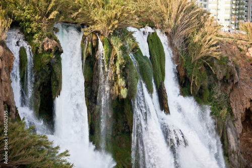 A waterfall erupts into the sea from a great height on a sunny day near the city