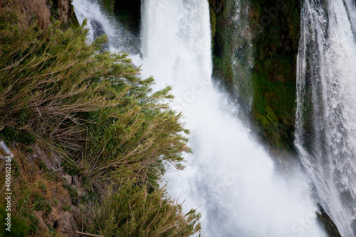 A waterfall erupts into the sea from a great height on a sunny day near the city