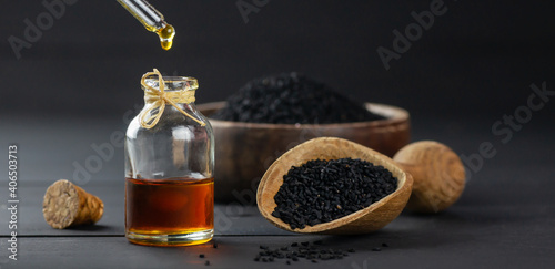 Glass bottle of black cumin seed essential oil , Nigella Sativa in scoop on black wooden background, oil dripping photo