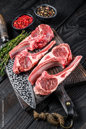Lamb chops raw meat on bone with salt, pepper and herbs. Black wooden background. Top view