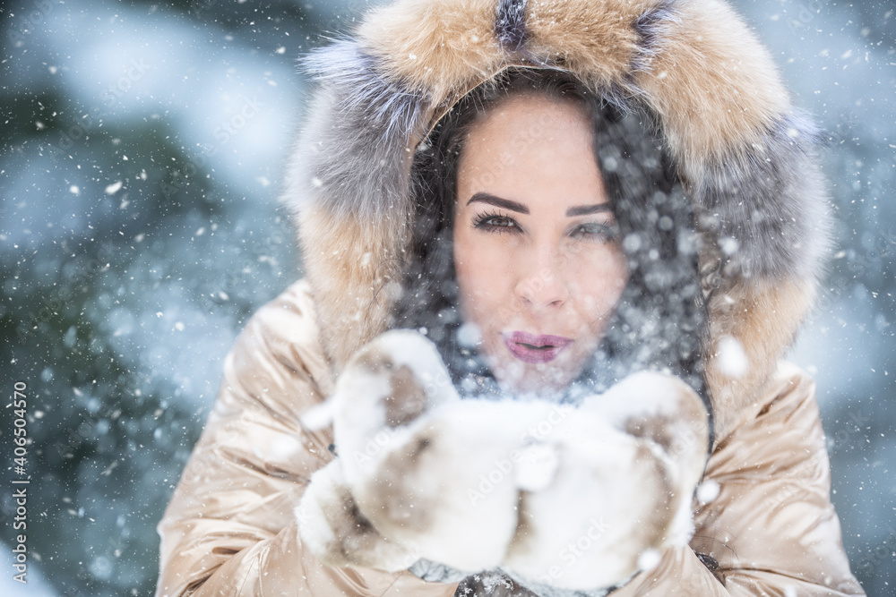 Good looking girl blows snow towards the camera dressed in furry warm clothes for the cold winter Good looking girl blows snow towards the camera dressed in furry warm clothes for the cold winter